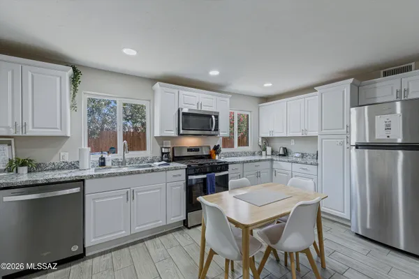 a kitchen with stainless steel appliances granite countertop a refrigerator a stove top oven a sink dishwasher and white cabinets with wooden floor