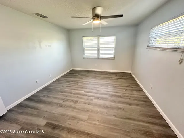 an empty room with wooden floor chandelier fan and windows