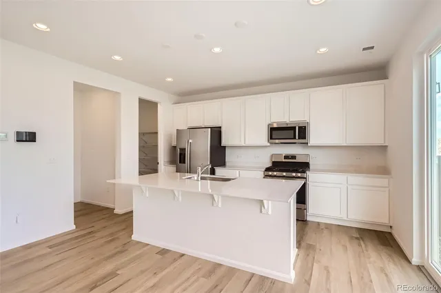 a kitchen with stainless steel appliances a microwave a stove a sink dishwasher a refrigerator and white cabinets with wooden floor