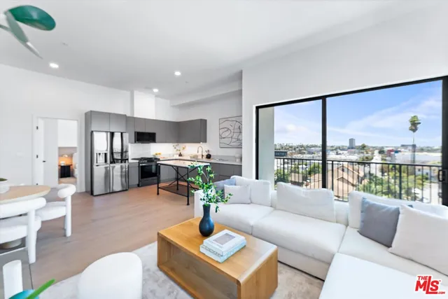 a living room with furniture wooden floor kitchen view and a large window