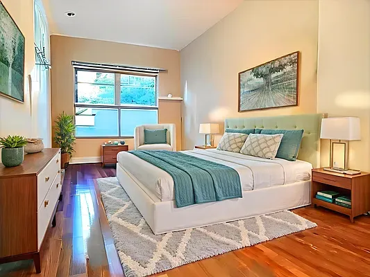 a bedroom with a bed and a lamp on dresser with wooden floor