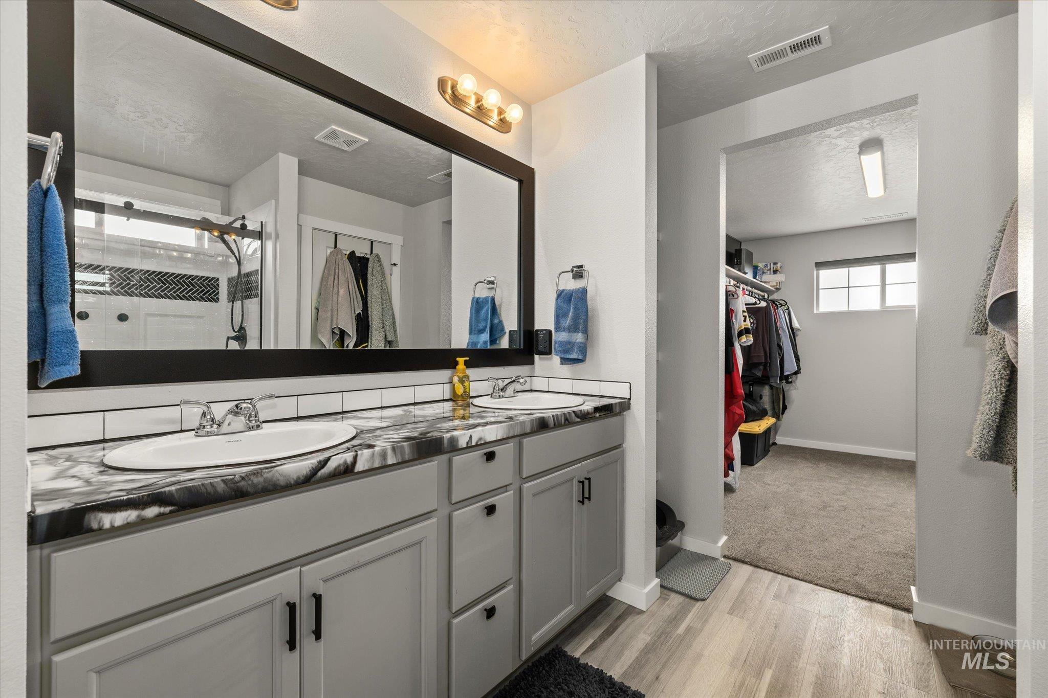 2024 Placerville Street Middleton, ID 83644 - Photo 22 of 38 Bathroom featuring double vanity, a walk in closet, light wood-type flooring, a stall shower, and a textured ceiling