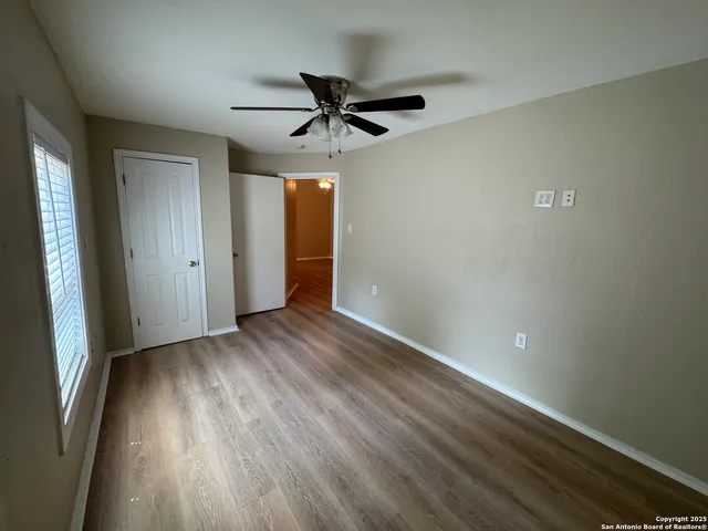 an empty room with wooden floor a ceiling fan and windows