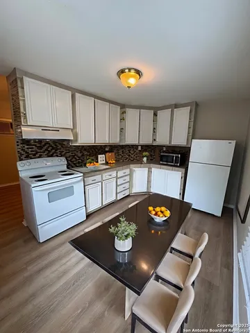 a kitchen with stainless steel appliances granite countertop a stove top oven a sink a dining table and chairs with wooden floor