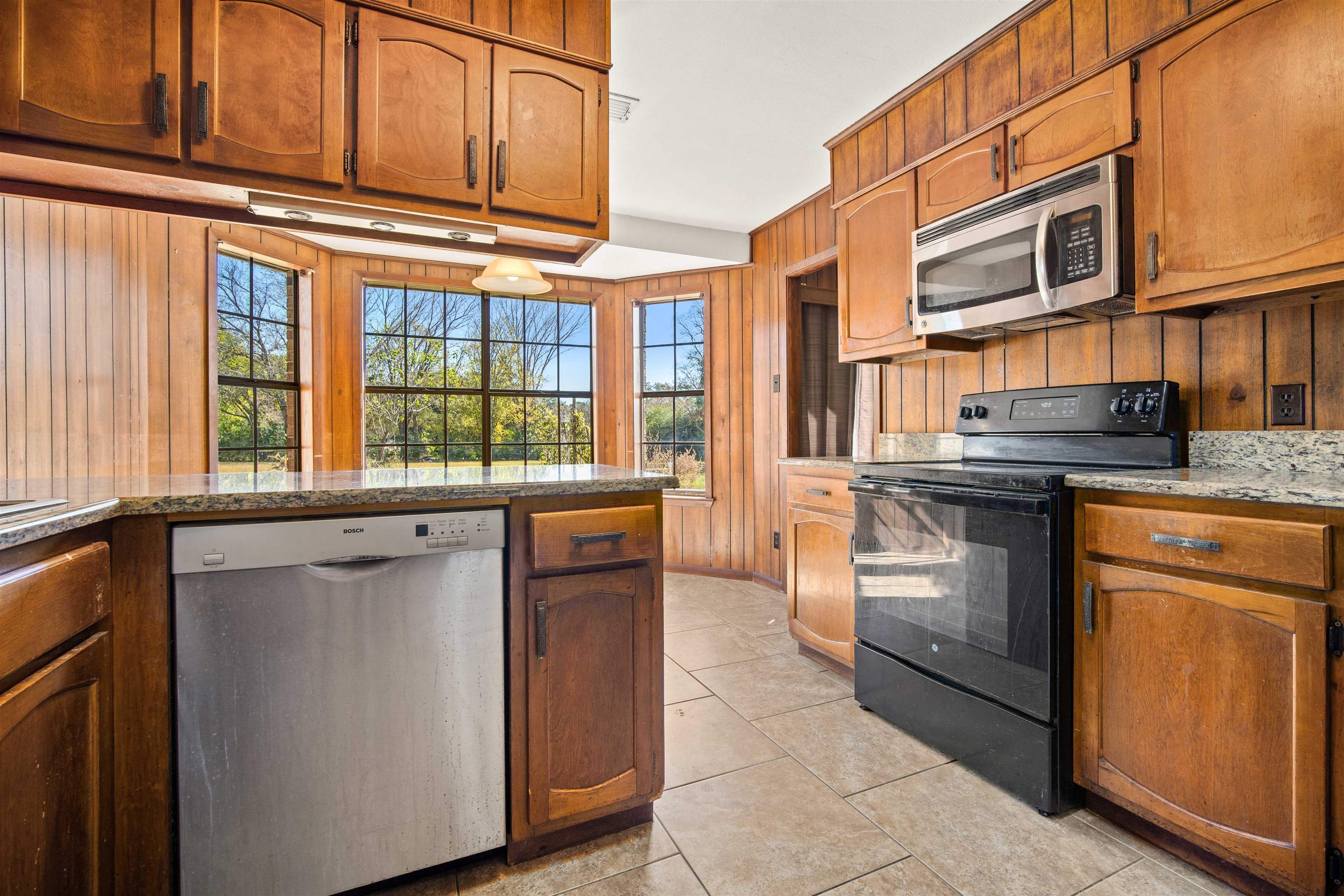 10285 Argyle Road Irvington, AL 36544 - Photo 10 of 28 Kitchen with wooden walls, stainless steel appliances, light stone countertops, light tile patterned floors, and brown cabinets