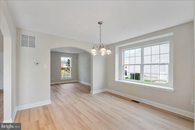 an empty room with wooden floor chandelier and windows