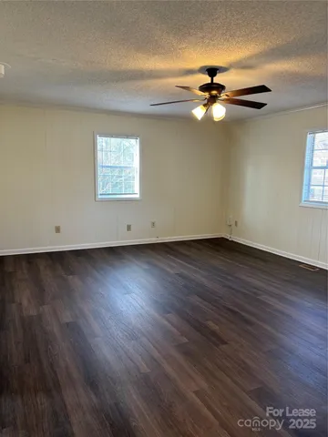 a view of an empty room with wooden floor and a ceiling fan