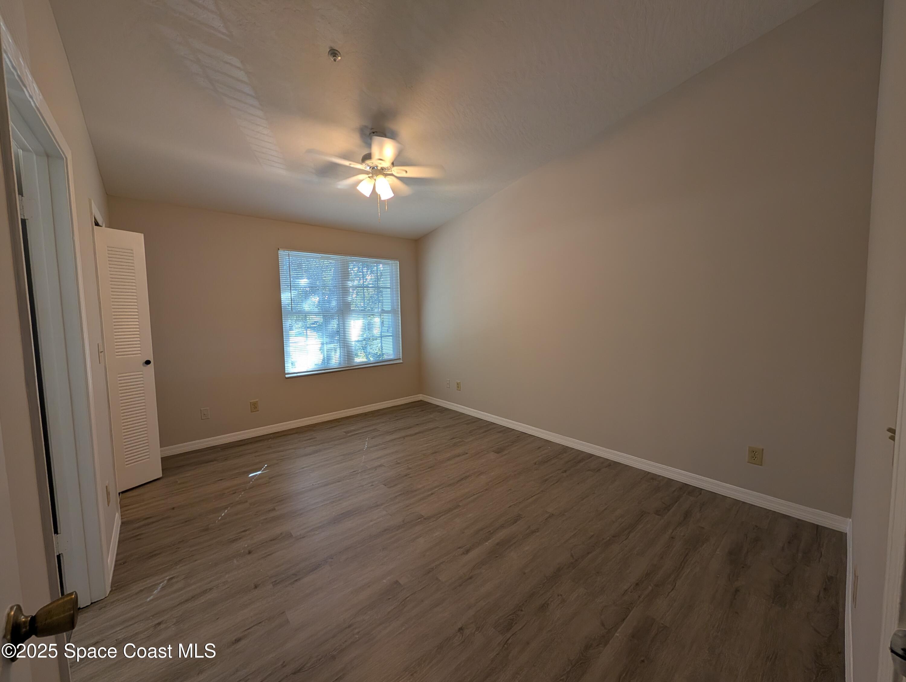 7667 North Wickham Road, Unit 1209 Melbourne, FL 32940 - Photo 8 of 23 an empty room with wooden floor chandelier fan and windows