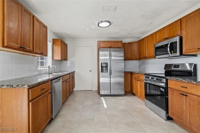 a kitchen with stainless steel appliances granite countertop a stove top oven a sink dishwasher and a refrigerator with wooden cabinets