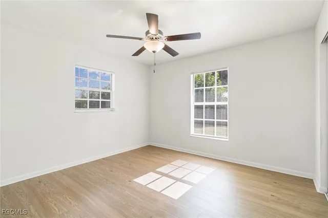 an empty room with wooden floor fan and windows