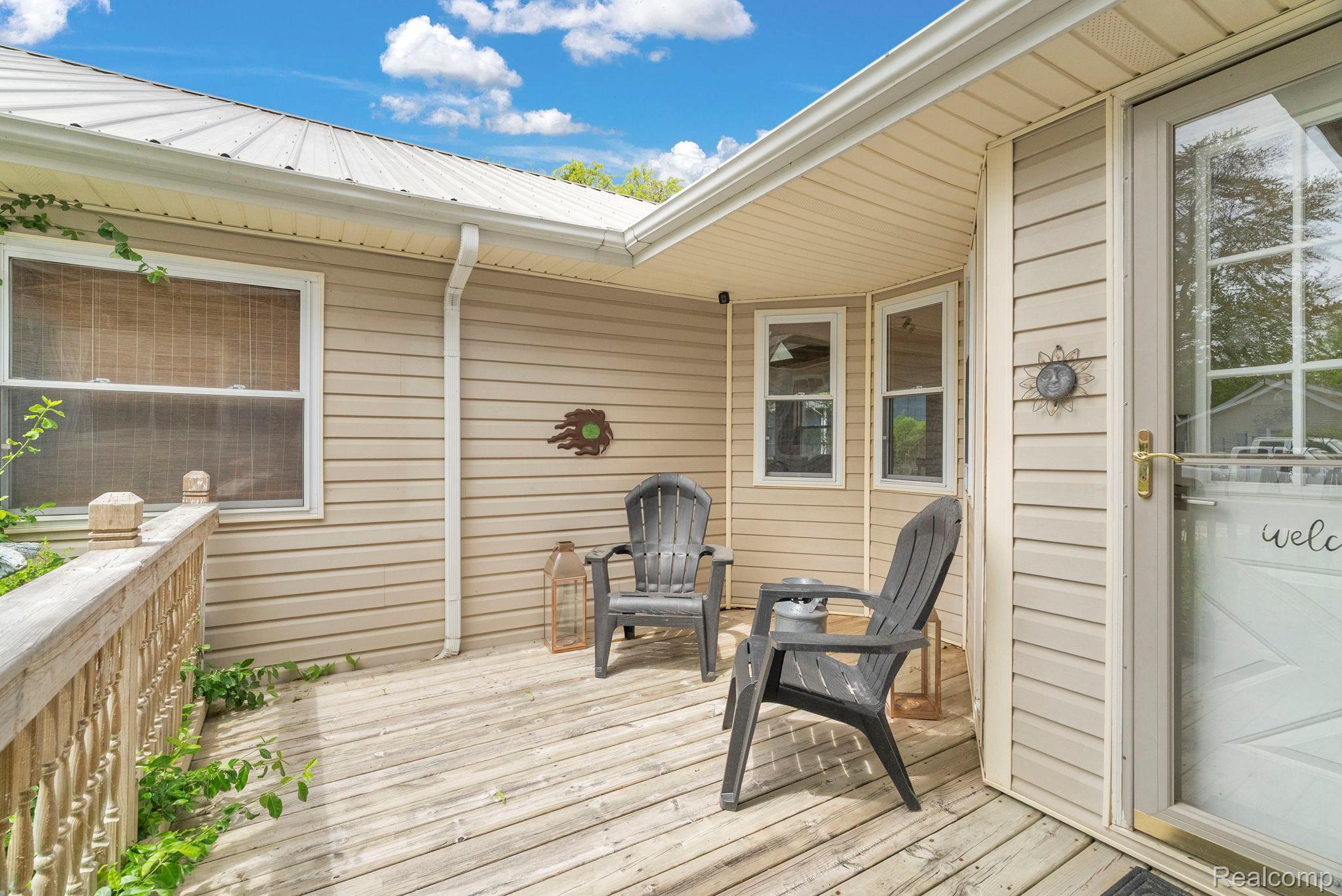 7489 Aspen Road Lexington, MI 48450 - Photo 8 of 62 Covered wood-plank deck with a railing, featuring beige vinyl siding, a metal roof, and an exterior door with a glass panel