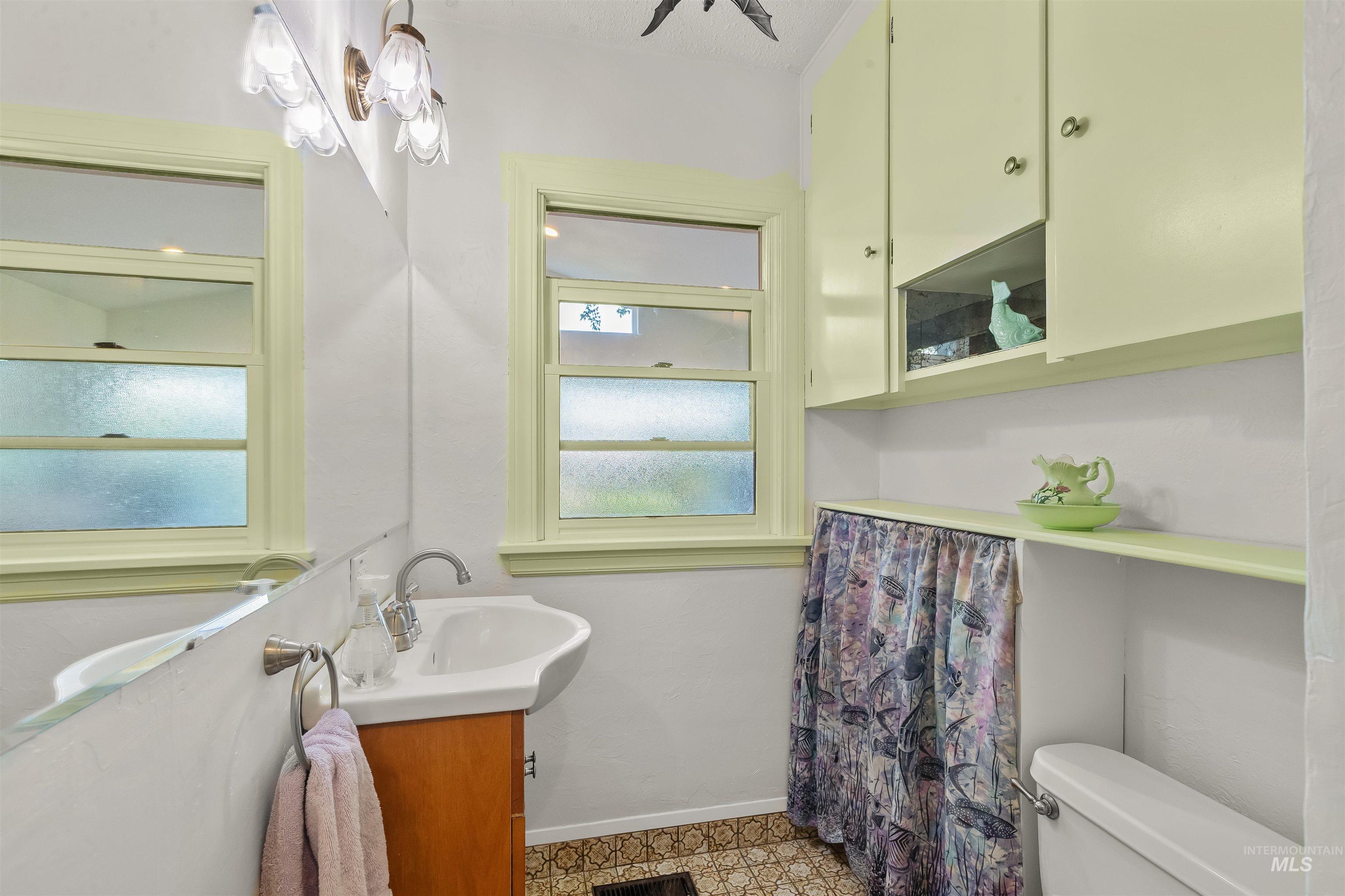 924 N Street Lewiston, ID 83501 - Photo 23 of 46 Bathroom featuring a pedestal sink with a wood-finish vanity, decorative wall sconce lighting, two casement windows with frosted glass, built-in wall cabinetry with display shelving, and patterned floor tiling