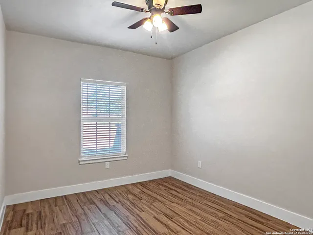 an empty room with wooden floor chandelier fan and windows