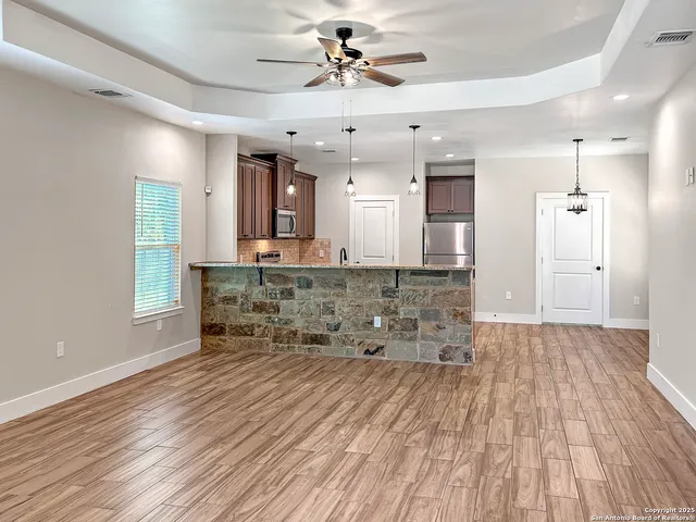 a living room with kitchen island granite countertop wooden floor and a refrigerator