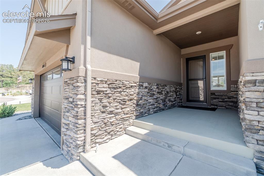 1061 Native Dancer Terrace Colorado Springs, CO 80921 - Photo 4 of 50 Inviting covered entry featuring a paneled front door with a full-light storm door, an adjacent window with blinds, and stone veneer accents