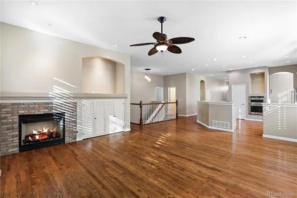 a view of a room with wooden floor a ceiling fan and kitchen view