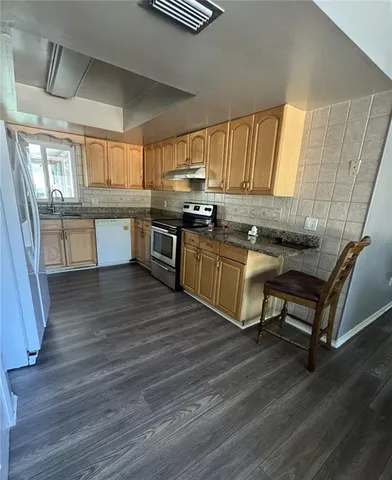 a kitchen with stainless steel appliances granite countertop a sink wooden cabinets and wooden floor