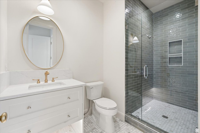 478 South Maple Lakes Drive Mapleton, UT 84664 - Photo 39 of 51 Bathroom featuring a walk-in shower with subway tile surround and built-in niches, glass shower enclosure, vanity with stone countertop, undermount sink, and brass-finish faucet, and a round frameless mirror