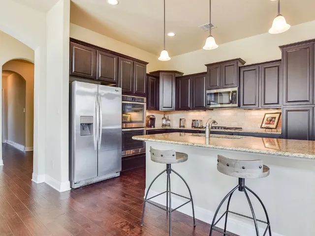 a kitchen with stainless steel appliances granite countertop a refrigerator a sink a stove a microwave and wooden floors