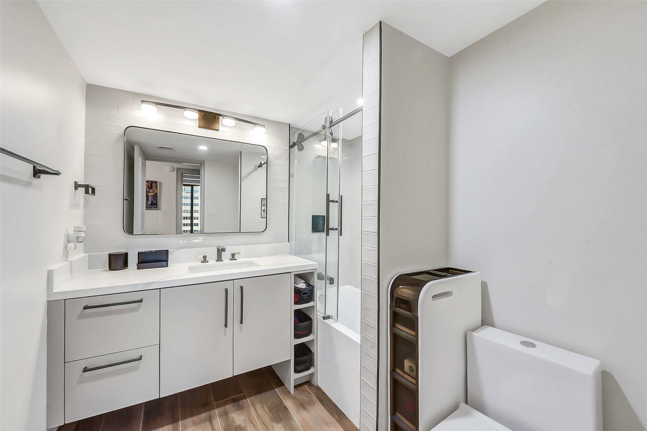 1111 Caroline Street, Unit 2903 Houston, TX 77010 - Photo 14 of 27 The second bath features a sleek white vanity, a large framed mirror, and a clean tub/shower combo. The warm wood-toned flooring provides a beautiful contrast to the bright, airy finishes
