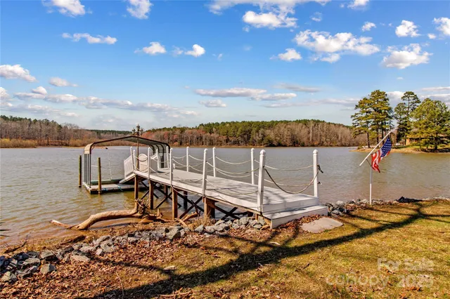 a view of a white house with a large pool and lawn chairs under an umbrella