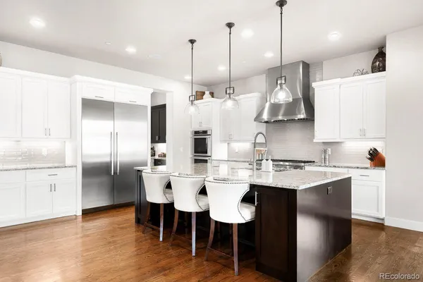 a kitchen with stainless steel appliances granite countertop a sink a stove a refrigerator and island with wooden floor