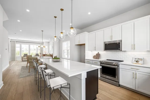 a kitchen with stainless steel appliances kitchen island granite countertop a stove a sink a microwave a dining table and chairs with wooden floor