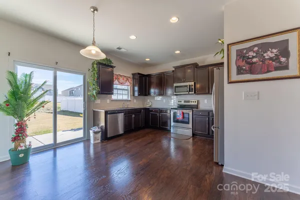 a kitchen with stainless steel appliances granite countertop wooden cabinets a refrigerator a sink a stove and a wooden floors