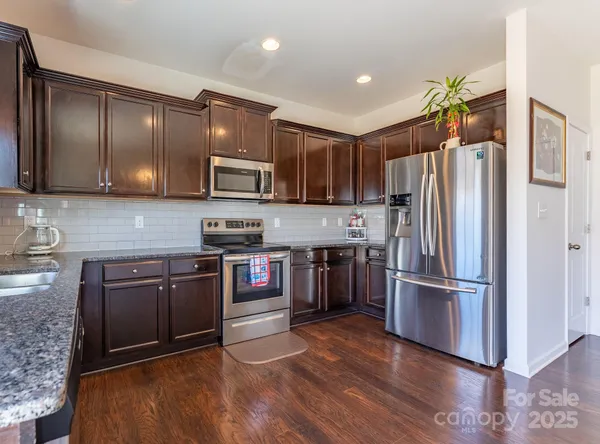 a kitchen with stainless steel appliances granite countertop a refrigerator a sink dishwasher a stove and a dining table with wooden floor