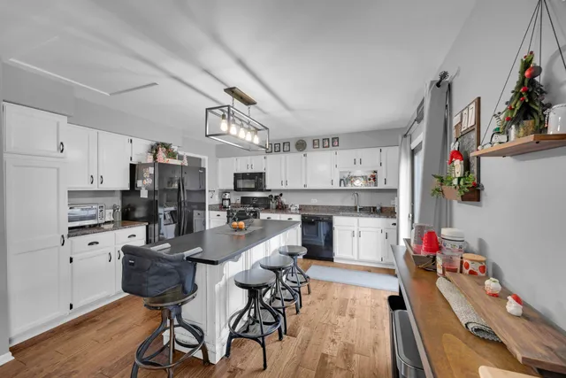 a kitchen with stainless steel appliances kitchen island granite countertop a refrigerator a stove a sink dishwasher and white cabinets with wooden floor