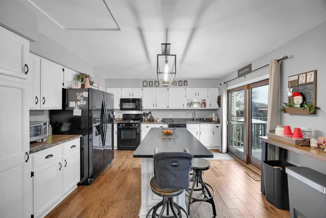 a large kitchen with stainless steel appliances kitchen island granite countertop a large stove a refrigerator a sink dishwasher and white cabinets with wooden floor