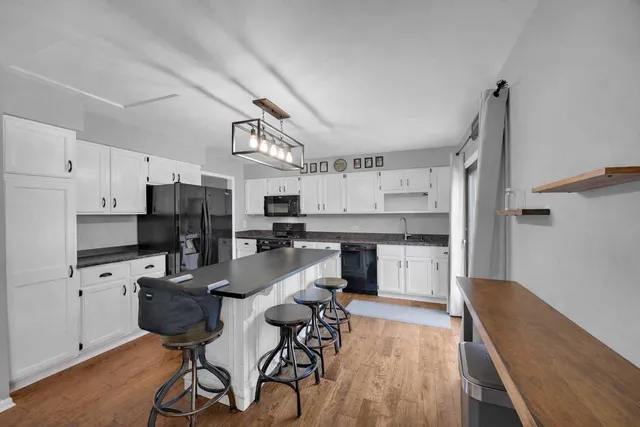 a kitchen with stainless steel appliances kitchen island granite countertop a refrigerator a stove a sink dishwasher and white cabinets with wooden floor