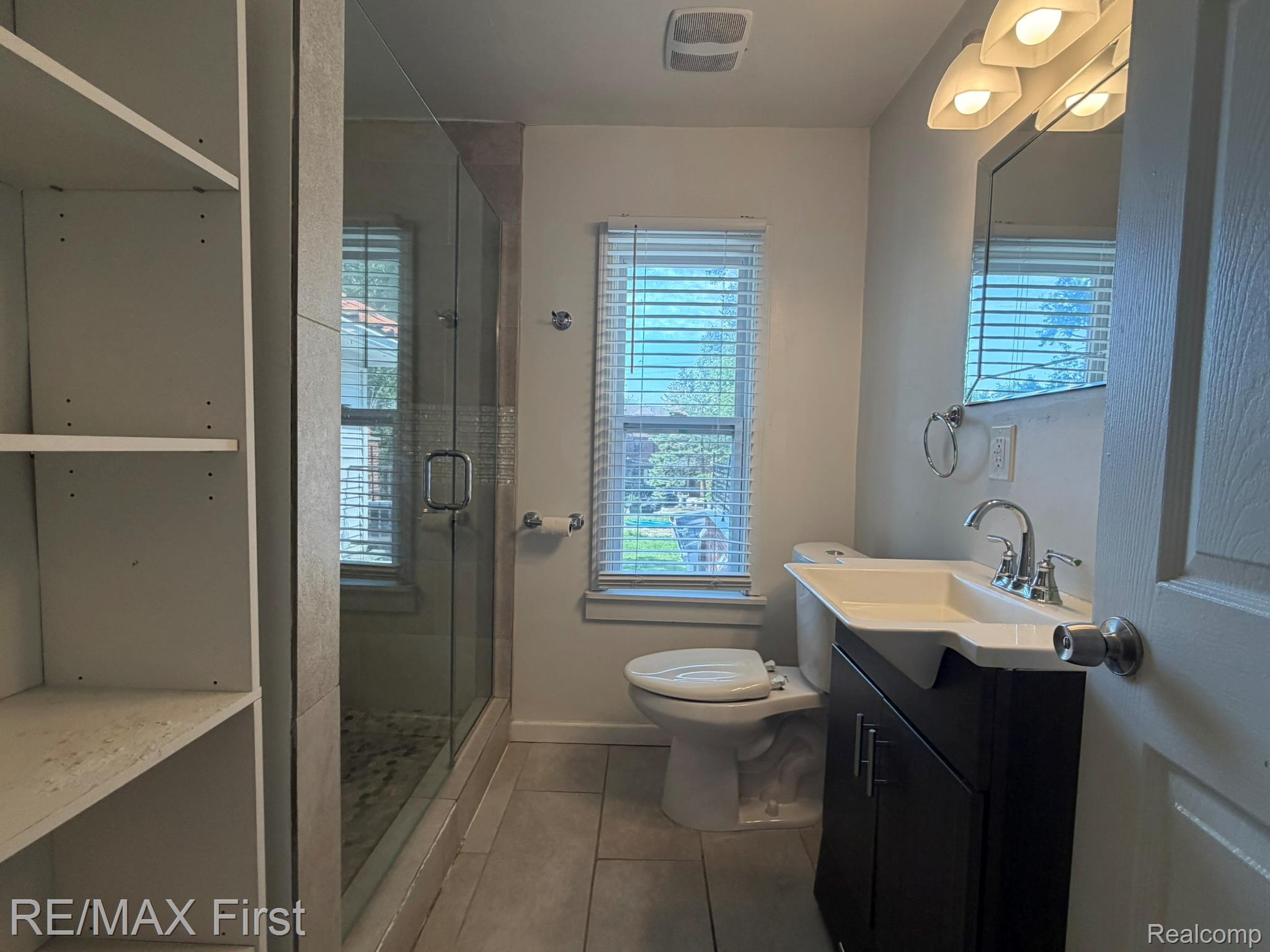 1349 Devonshire Road Grosse Pointe, MI 48230 - Photo 22 of 31 Walk-in shower with clear glass enclosure, freestanding vanity with integrated sink, modern wall-mounted light fixture, built-in shelving, and tiled flooring