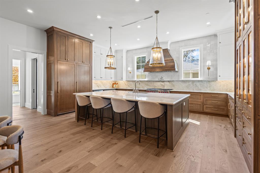 5925 Williamstown Road Dallas, TX 75230 - Photo 8 of 39 Kitchen with a kitchen bar, a large island with sink, brown cabinetry, light stone counters, and pendant lighting