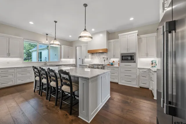 a kitchen with stainless steel appliances kitchen island granite countertop a table chairs and a refrigerator