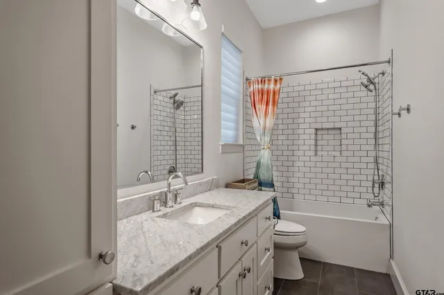 a bathroom with a granite countertop toilet a sink a mirror a bathtub and shower