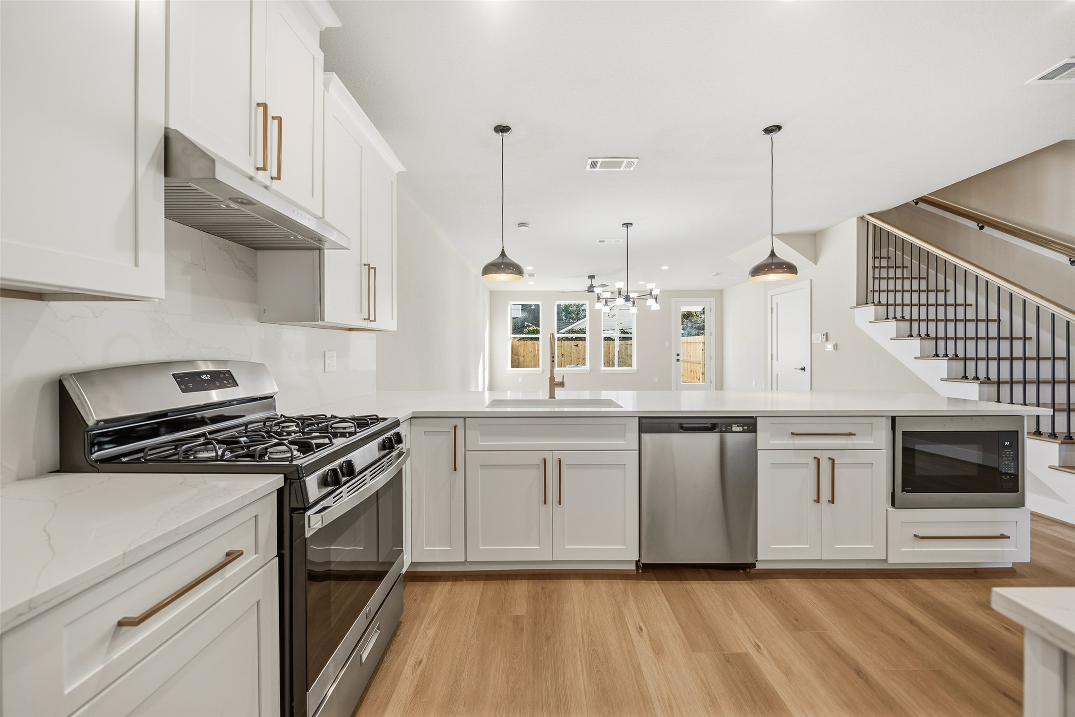 3422 Elser Street Houston, TX 77009 - Photo 6 of 26 This modern kitchen features sleek white cabinetry, stainless steel appliances, and a spacious island with pendant lighting. The open layout flows into a bright dining area with large windows, and there's a stylish staircase in the background.