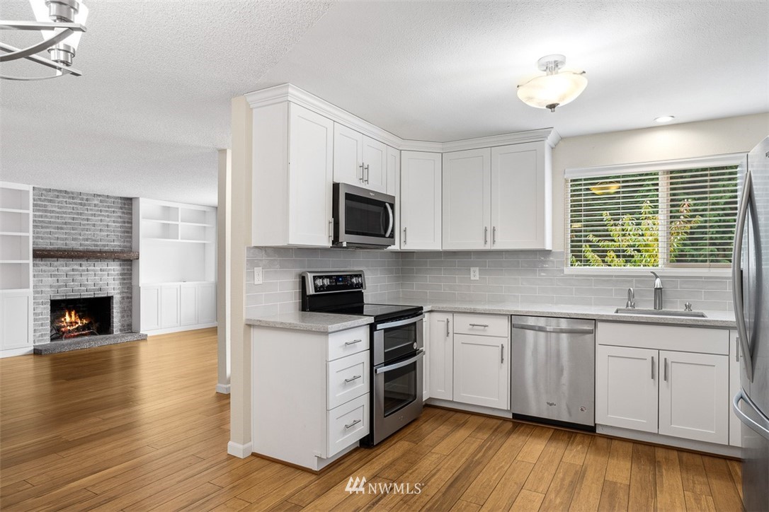 16505 23rd Avenue Southeast Bothell, WA 98012 - Photo 12 of 33 a kitchen with stainless steel appliances granite countertop a stove top oven a sink dishwasher and a fireplace with wooden floor