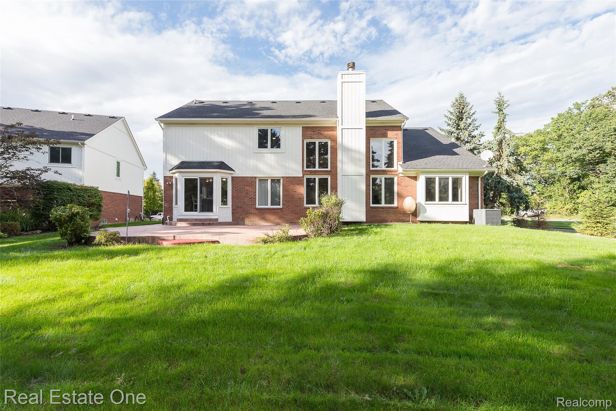 1013 Rochelle Park Drive Rochester, MI 48307 - Photo 67 of 74 Expansive green lawn with a red brick and white siding exterior, featuring multiple windows, a bay window, and a patio