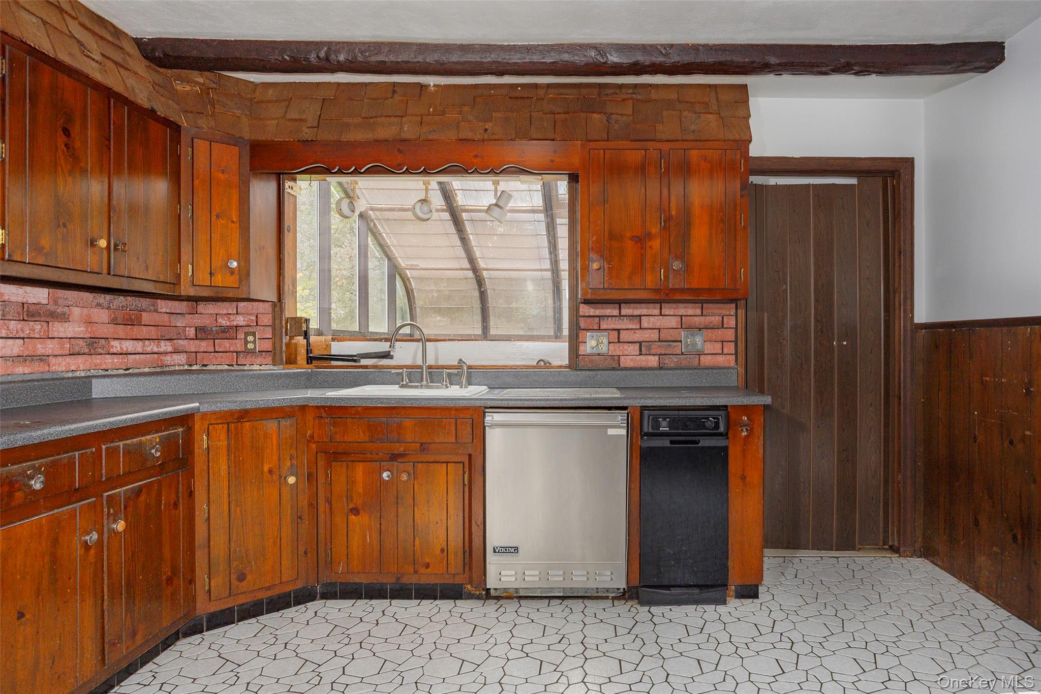 993 Highway 32 Wallkill, NY 12589 - Photo 21 of 35 Kitchen with dark countertops, stainless steel dishwasher, wood walls, tasteful backsplash, and brown cabinets