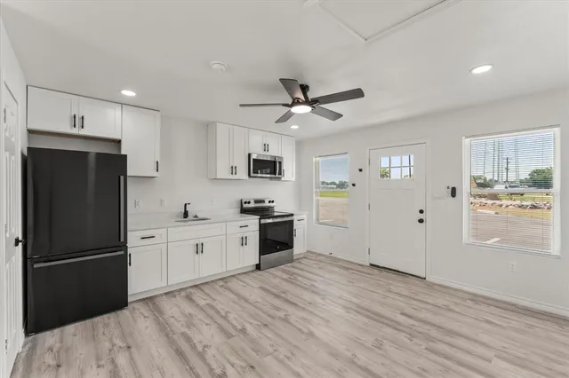 a kitchen with granite countertop a refrigerator oven a sink dishwasher and white cabinets with wooden floor