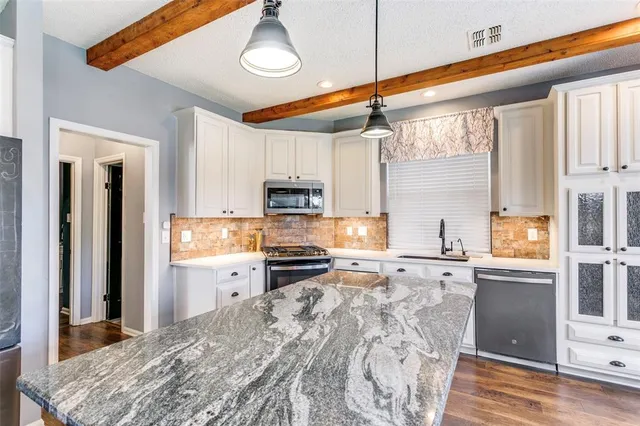 a kitchen with stainless steel appliances granite countertop a refrigerator a sink dishwasher a stove and white cabinets with wooden floor