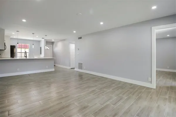 an empty room with wooden floor and a kitchen