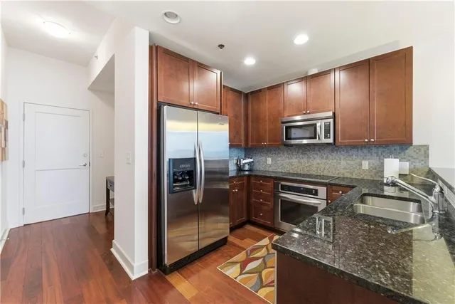 a kitchen with stainless steel appliances granite countertop a refrigerator a stove and a sink with wooden floor