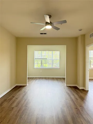 an empty room with wooden floor chandelier fan and windows
