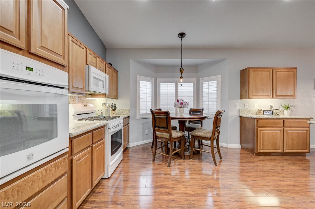 1604 Cattle Ranch Place Henderson, NV 89002 - Photo 20 of 99 A warm kitchen with rich wood flooring and cabinets, showcasing white appliances and a cozy bay window dining nook.