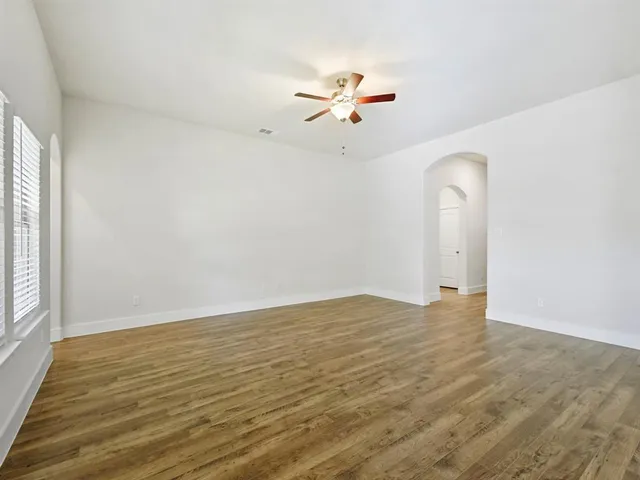 an empty room with wooden floor fan and windows