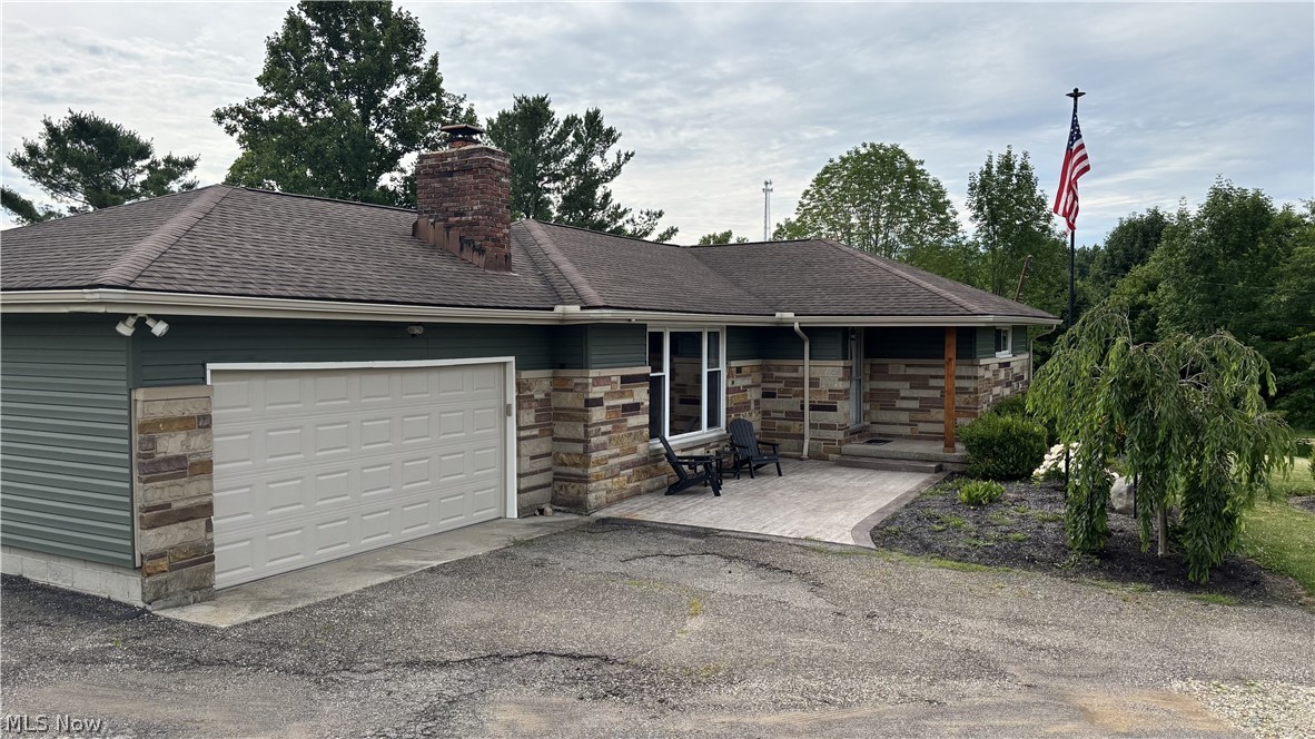 11784 Chamberlain Road Mantua, OH 44255 - Photo 39 of 50 Charming ranch-style home featuring a detached garage with white overhead door, stone and siding exterior, covered front porch entry, mature landscaping with established trees and shrubs, and an American flag mounted on the property