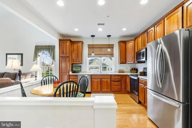 a kitchen with stainless steel appliances granite countertop a refrigerator a sink dishwasher a stove and a dining table with wooden floor