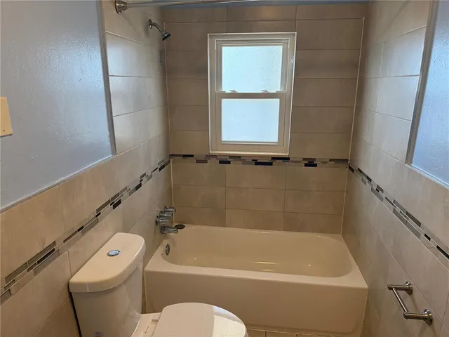 a bath tub sitting next to a white toilet and a window